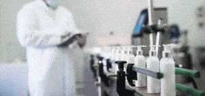 bottle of lotions being manufactured with worked in the background looking at a clipboard checking business operations