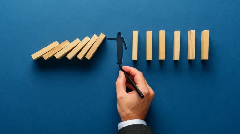 Silhouette of a man making a stop gesture to prevent wooden dominoes from collapsing