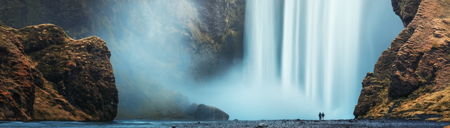 Two people at the foot of a large waterfall